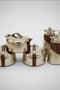 Set of silver containers with brown straps on a stone surface with a garden background